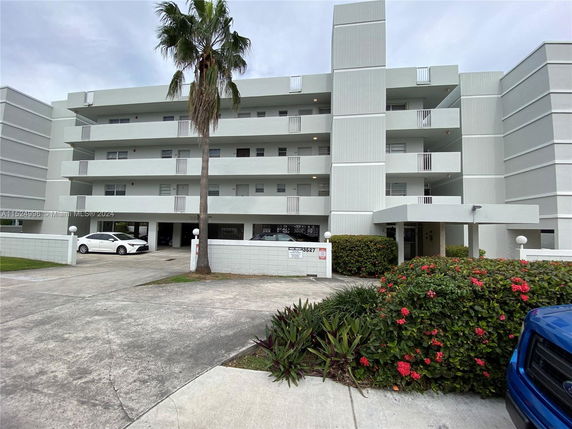 Front view of a multi-story building with balconies and parking area.