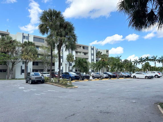 Outdoor parking area in front of a multi-story residential building with palm trees.