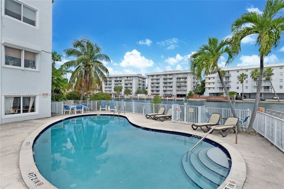 Outdoor swimming pool area with lounge chairs and nearby buildings.