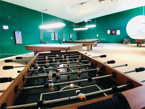 Room with foosball and pool tables, green walls, and dartboard.