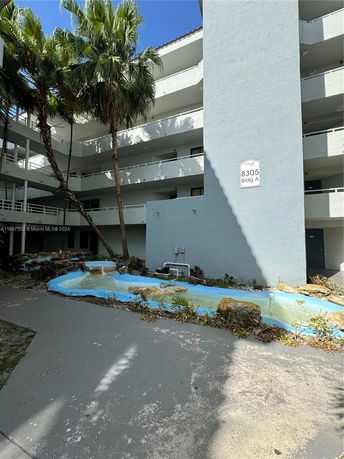 View of a multi-story building with balconies and palm trees in front.