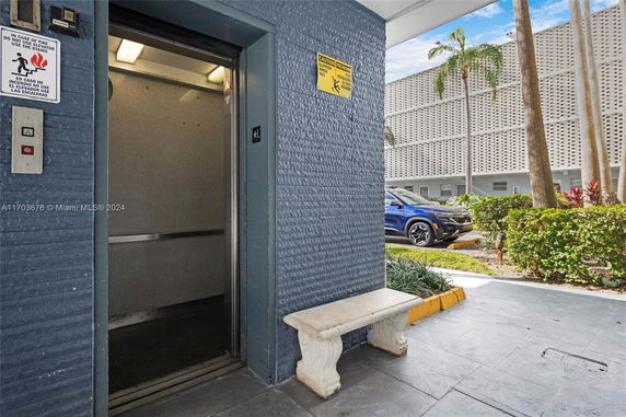 Elevator door open to a landscaped area with a parked car and building in the background.