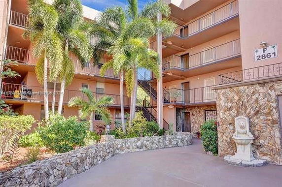 Outdoor view of a multi-story building with balconies and palm trees in the courtyard.