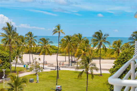 View of palm trees and a beach in the background from a balcony.