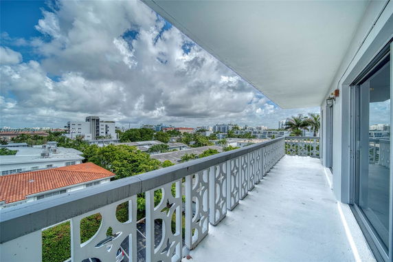 View from a balcony overlooking a cityscape with buildings and trees under a cloudy sky.
