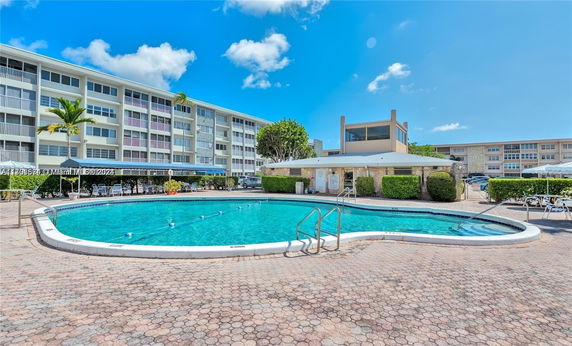 Outdoor swimming pool area with multi-story residential building in the background.