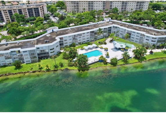 Aerial view of a large residential building near a body of water, with a swimming pool and landscaped grounds.