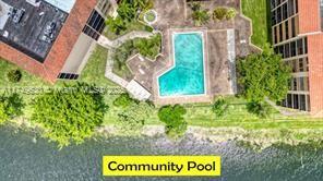 Aerial view of a community swimming pool next to buildings, surrounded by greenery.