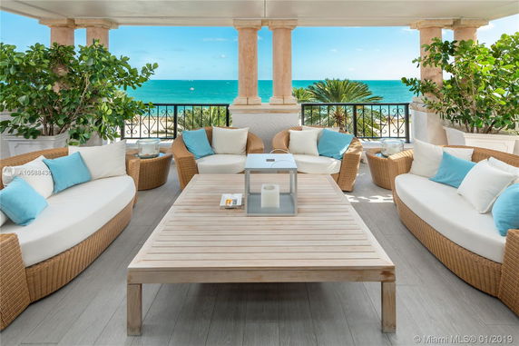 Outdoor patio overlooking the ocean with wicker furniture and decorative pillars.