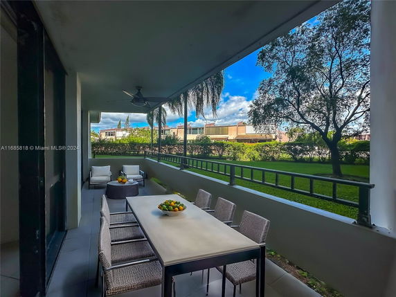 Covered outdoor patio area with seating and dining table, overlooking a grassy yard and trees.