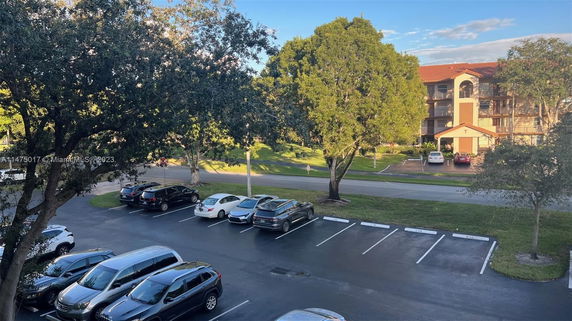 Outdoor parking area with several parked cars and a multi-story building in the background.