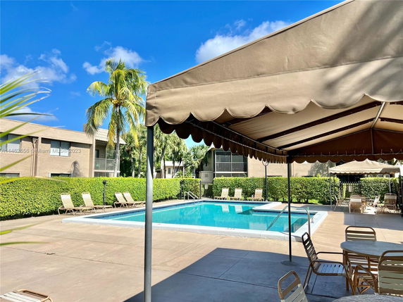 Outdoor swimming pool area with lounge chairs and shade canopy.