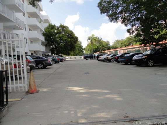 Outdoor parking area with multiple parked cars beside a multi-story building.