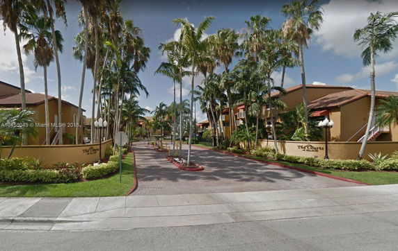Front view of a gated residential complex with palm trees and a paved driveway.