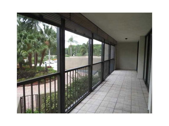 View from a covered balcony with tiled flooring and metal railings overlooking palm trees and a pathway.