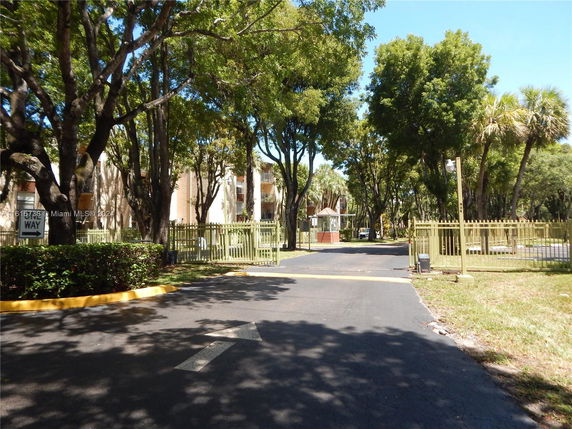 Entrance view of a gated community with multiple residential buildings surrounded by trees.