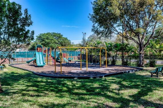 Playground with slides and swings surrounded by trees and a fence.
