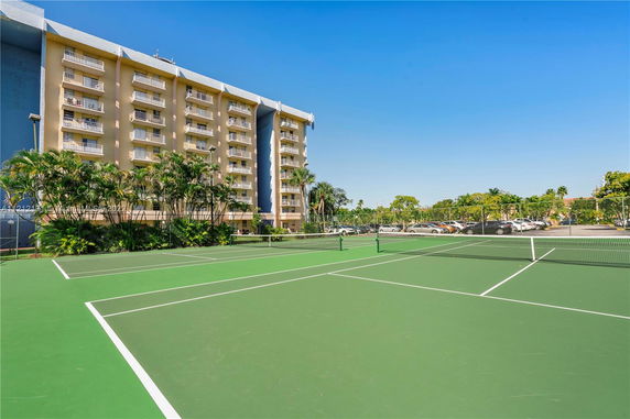 View of a multi-story residential building with balconies, adjacent to a tennis court.