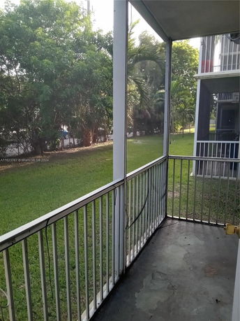 View from a building showing a balcony with metal railing and a grassy area with trees.