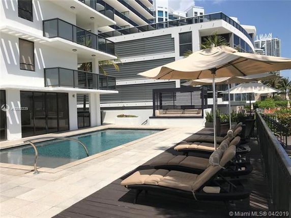 Outdoor swimming pool area with lounge chairs and umbrellas next to a multi-story building.
