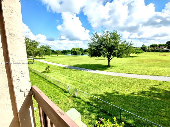 View from a building showing a grassy area with a tree and a path, under a partly cloudy sky.