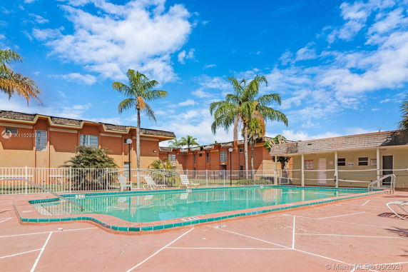 Outdoor swimming pool area with surrounding buildings and palm trees.