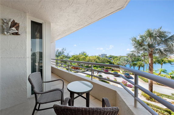 Balcony view with seating area overlooking lush greenery and water.