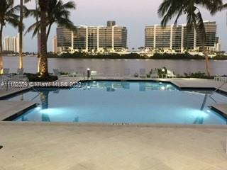 View of high-rise buildings across a body of water with a pool and palm trees in the foreground.