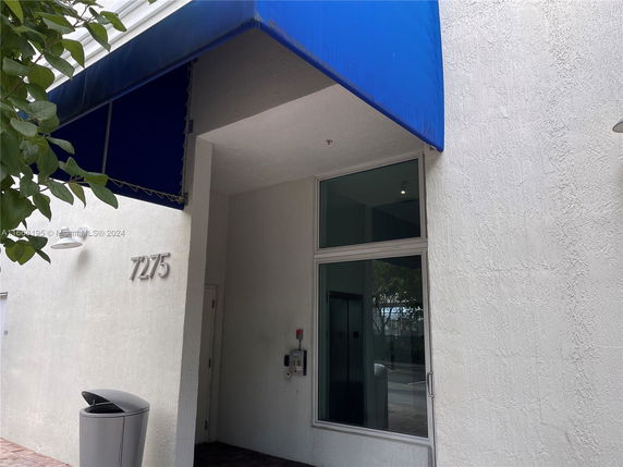 Exterior view of a building entrance with a blue awning and the number 7275 displayed.