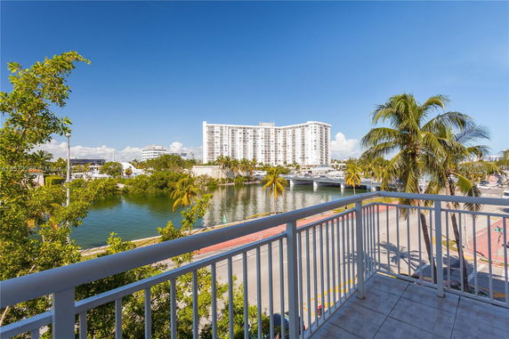 View of a multi-story building across a body of water, with palm trees and waterfront areas visible.