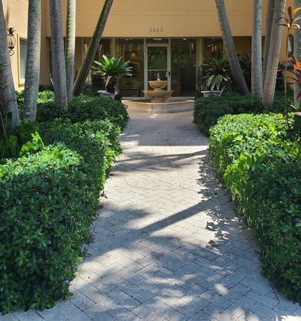 Front view of a building entrance with landscaped walkway and glass doors.