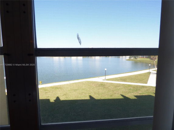 View through a window showing a lake and grassy area with pathways and lampposts.