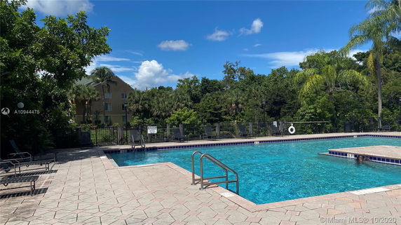 Outdoor swimming pool with trees and a building in the background.