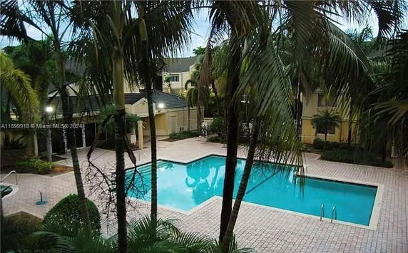 Outdoor swimming pool area surrounded by palm trees and buildings.