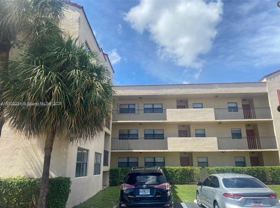 Front view of a three-story residential building with balconies and parking area.