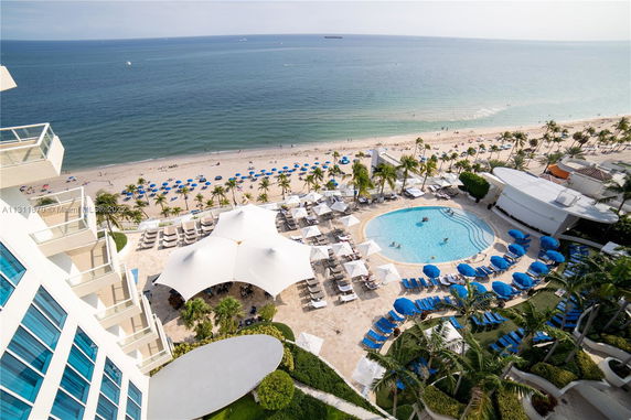 View of a hotel overlooking a beach with a poolside area featuring umbrellas and lounge chairs.
