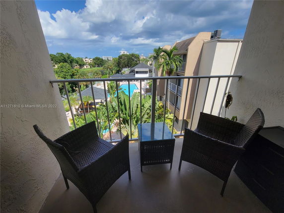 View from a balcony overlooking a swimming pool and surrounding greenery.