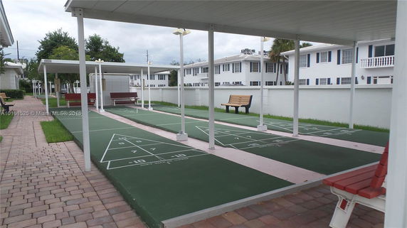 Outdoor area with shuffleboard courts and benches, covered by canopies.