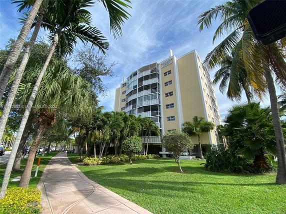 Front view of a multi-story residential building with balconies and surrounded by palm trees.