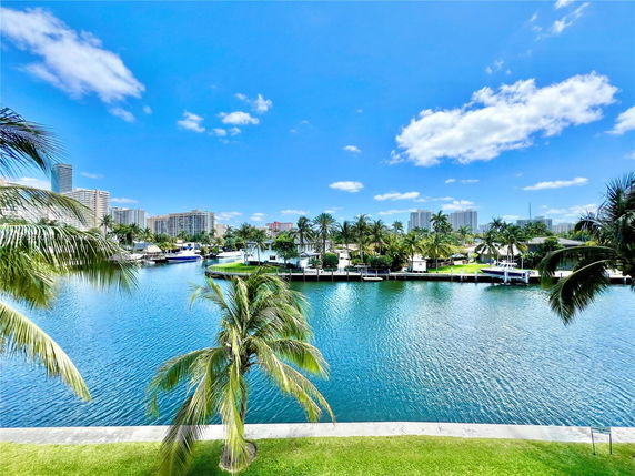 Panoramic view of waterfront with palm trees and buildings in the distance.