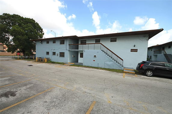 Front view of a two-story building with an outdoor staircase and parking area.