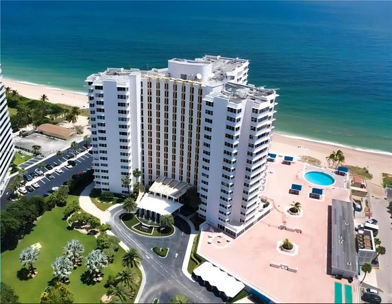 Aerial view of a beachfront high-rise building with parking area and swimming pool.