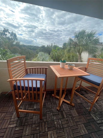 Outdoor seating area with wooden furniture overlooking greenery and palm trees.