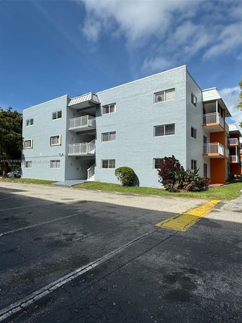 Front view of a three-story apartment building with balconies and a parking area.