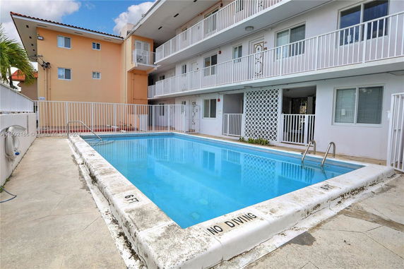 Outdoor swimming pool next to a multi-story building with balconies.