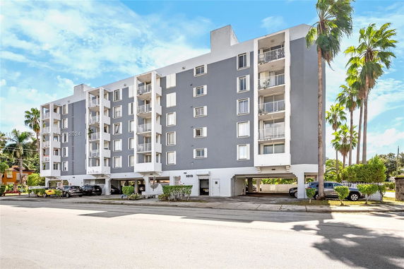 Front view of a multi-story apartment building with balconies and ground-level parking.
