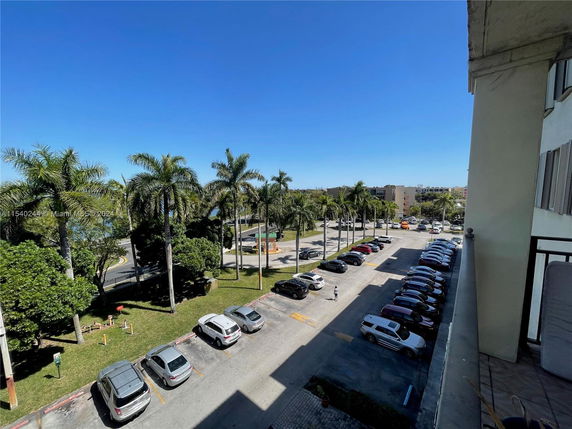 View from a building overlooking a parking area with several cars and palm trees in the background.
