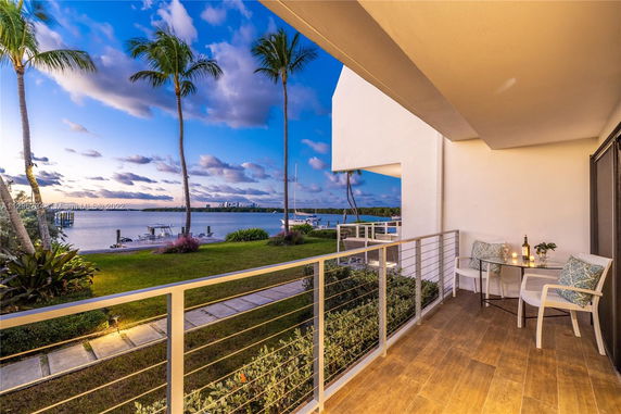 Outdoor balcony view overlooking a body of water with palm trees.