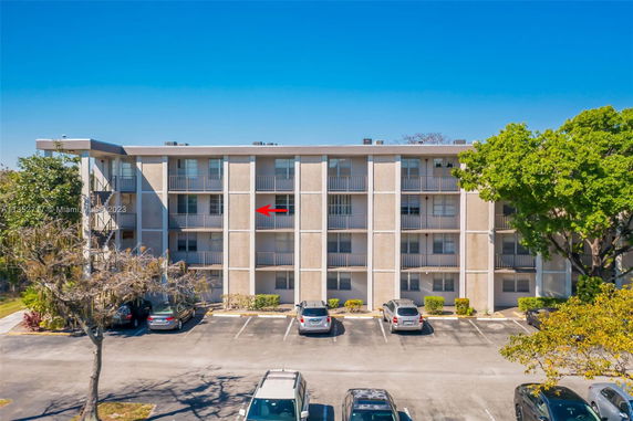 Front view of a multi-story apartment building with balconies and a parking area in front.