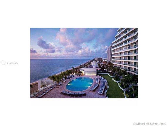 View of an outdoor pool area adjacent to a high-rise building, overlooking the ocean.